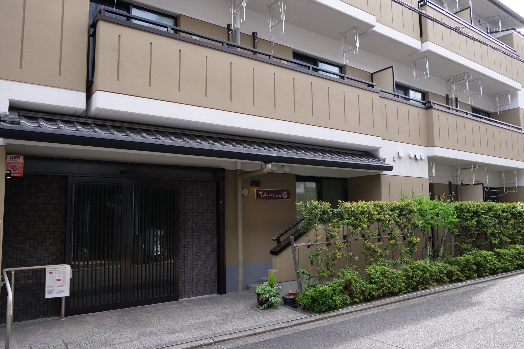 介護施設の玄関・車寄せ。黒い引き戸と緑の生垣が配置された入口。